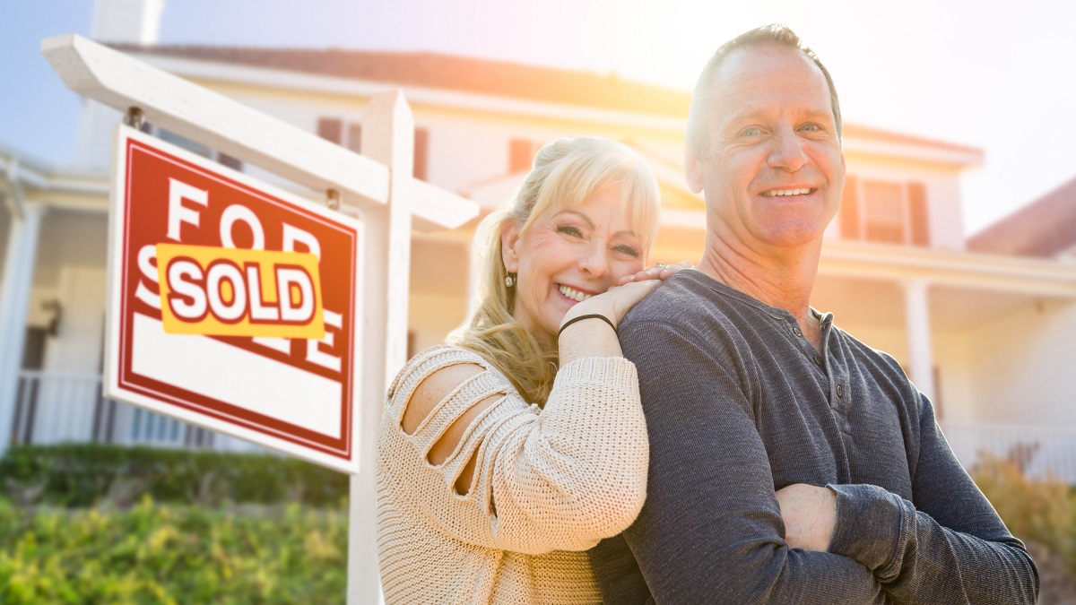 Attractive Middle-aged Couple In Front House and Sold Real Estate Sign.